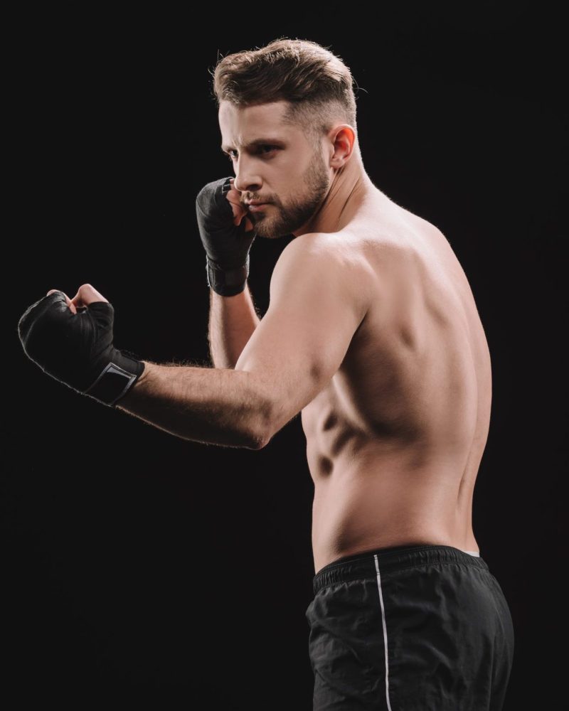 strong muscular mma fighter in bandages doing punch isolated on black